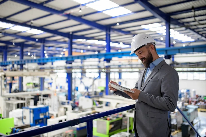 Manager in a hard hat reviewing a tablet in a manufacturing facility