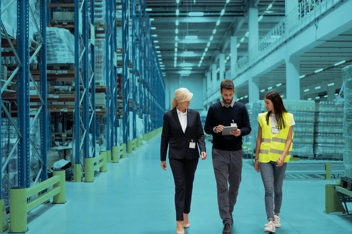 Three people walking through a warehouse reviewing inventory on a tablet